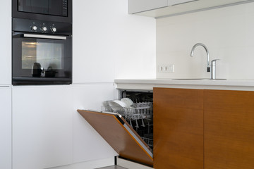 Opened modern dishwasher machine with plates and cups on kitchen