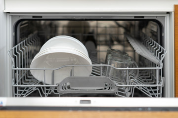 Opened modern dishwasher machine with plates and cups on kitchen