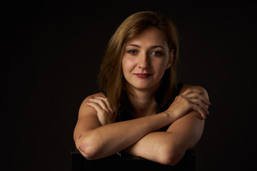 Cheerful girl with a smile and a peeled elbow on a chair. Leather sexy yolk. Portrait on a black background.