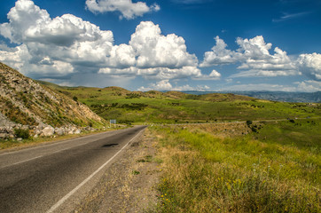 View of the road located high in the mountains of the Gegham Range against the background of a blue sky covered with clouds in Armenia