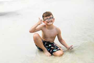 Little Boy Playing in the Sand on the Beach in Florida During the Summer making a thunbs up sign