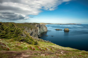 Pristine coastal seascape with soft clouds and sea stacks in beautiful clear blue water. Skerwink trail located in Port Rexton, Newfoundland Canada. 