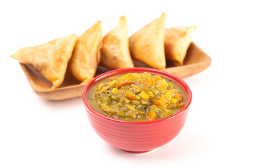 Spicy Vegetable Curry Isolated on a White Background with Samosas in the Background