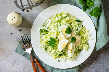 Healthy salad. Vegan salad with cabbage, eggs, cucumber, coriander and mayonnaise-mustard dressing on a light stone or slate table. Top view flat lay background.
