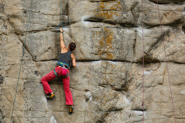 A young woman with a rope engaged in the sports of rock climbing on the rock.