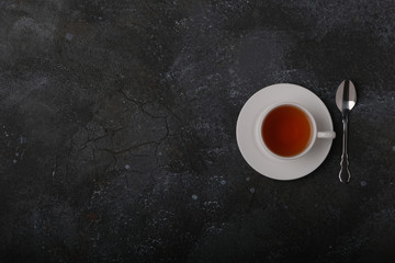 Obraz na płótnie Canvas white cup with tea and spoon on a dark background.