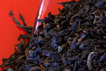 Black Chinese tea is poured out of a glass jar on a red surface. Imperial drink. Close-up. Background and backdrop