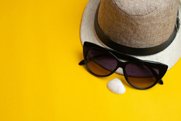 Summer accessories, sea shell, hat and sun glasses on yellow background. Summer vacation and sea concept.