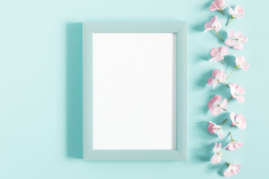 Beautiful flowers composition. Light pink flowers, empty photo frame for text on pastel blue background. Wedding. Birthday. Valentines Day. Mother's day. Flat lay, top view, copy space