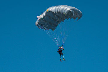 Skydiver with grey parachute in blue sky