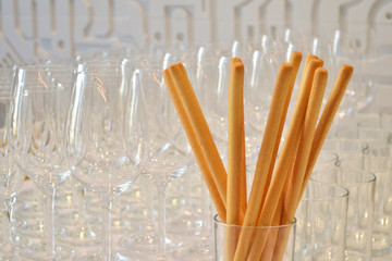 Breadsticks stand in clear glass at a party, behind are empty glasses