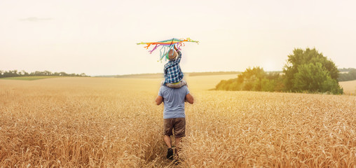 Happy father and son flying kite in the field at sunset