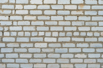 White old rough brick wall background. Careless masonry from second-grade damaged white silicate brick.