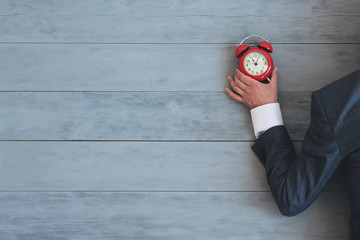 Tired overworked businessman with a red alarm clock in his hand is sleeping on an office floor background with copy space.