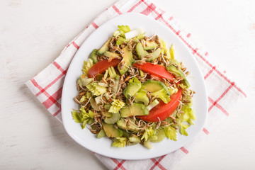 Vegetarian salad of celery, germinated rye, tomatoes and avocado on linen tablecloth, top view.
