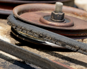 An old, cracked drive belt and pulley on a lawn mower deck needing maintenance