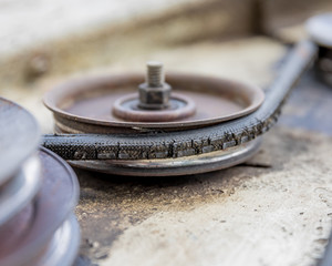 An old, cracked drive belt and pulley on a lawn mower deck needing maintenance