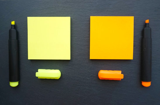 Sticky notes in yellow and orange color with marker pens in the same color on the black board background