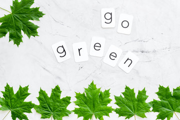 Go green text with green maple leaves on marble background top view