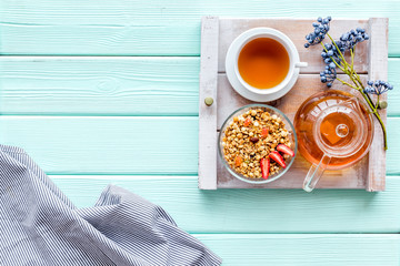 Breakfast in bed with granola, tea in pot and cup on tray on mint green wooden background top view - Powered by Adobe