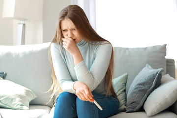 Obraz premium Sad young woman with pregnancy test at home