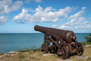 Old antique cannon at Fort James on the edge of a cliff with lots of clouds in the sky, Antigua