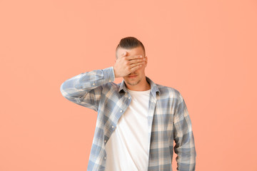 Young man covering his eyes on color background