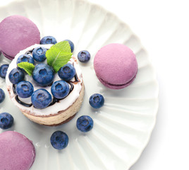 Plate with tasty blueberry cake with macarons on white background