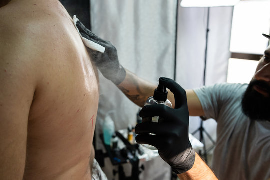 tattoo studio salon preparing for tattooing back tattoo artist master professional applying alcohol to customers back