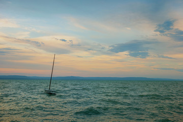 Small sailboat without sail on the stormy lake Balaton at sunset in Hungary - obrazy, fototapety, plakaty