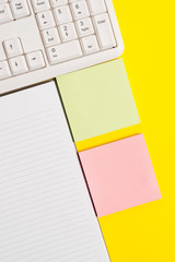 Colored empty papers with copy space on the yellow background table with pc keyboard.
