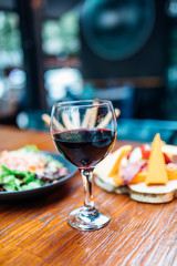 Dinner in the restaurant with Wine, Cheese and salad. Red wine glass, assorted cheese plate and smoked salmon salad on wooden dining table. This is Lunch or Dinner Restaurant or Cafe Concept Image.