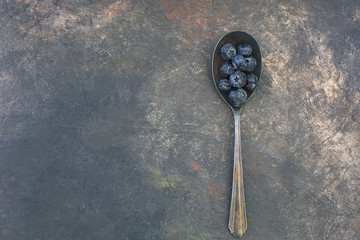 Freshly picked blueberries piled in an old tarnished spoon on a textured and predominatly black background.