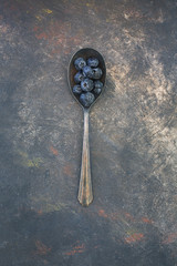 Freshly picked blueberries piled in an old tarnished spoon on a textured and predominatly black background.