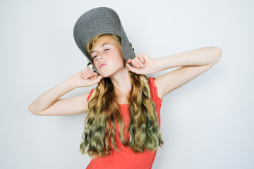 Funny teen girl with  green dyed curly long hair. Millennial generation concept. Caucasian girl in hat and red dress posing on grey background.