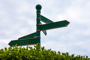 Green road sign on the crossroads with blue cloudy sky and green grass in the background.