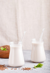 Organic non dairy buckwheat  milk in glass and wooden plate with buckwheat seeds on a gray concrete background.