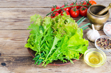 Green salad ingredients organic lettuce, cherry tomatoes, spices and olive oil on wooden background. 