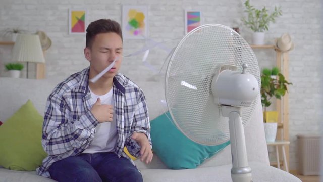 Young asian man sitting in front of a working fan, the concept of heat slow mo