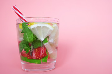 Summer bar concept. Glass of drink on pink background. Copy space. Summer cocktail with gin, mint leaves and fruit slices (strawberry, lemon, lime).