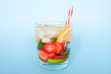 Glass of fruit water with slices of strawberry, lemon, lime and mint leaves. Refreshing summer drink on blue background.