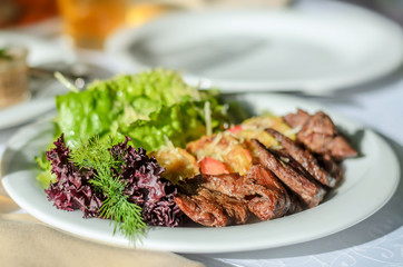 Roasted meat with garnish and fresh lettuce leaves on a white plate. Close-up, selective focus