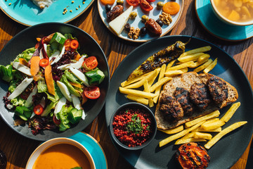 Dinner or lunch foods on wooden table from top view. Grilled or roasted meatballs, french fries, salad, snacks and soup. Dining dish table. 