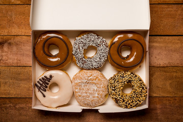 An open box of doughnuts on wooden table looks tasty with a variety of flavours