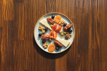 Traditional Ramadan fasting iftar snacks foods on the table. This is dates, dried apricots, black olives, tomatoes and cheese in plate on the wooden table. Snack plate.