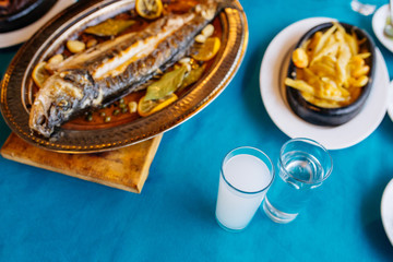 Turkish or Greek restaurant table and food dinner cuisine culture from top view. Traditional Greek ouzo or turkish raki with grilled or fried fish and appetizers on dinner table at restaurant. 