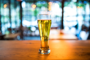 Glass of beer on old wooden table in cafe, restaurant or bar. Nightlife concept image. Cold Beer glass on the wooden desk in the retro vintage bar interior. This beer is draught and lager. 