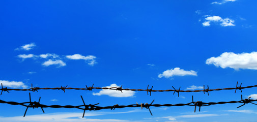 close up barbed wire fence over sunny blue sky