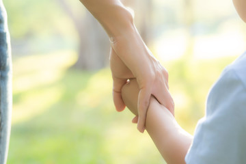 Closeup mother or parent and son holding hand with love together in summer outside in the park, mom take care kid holding palm with affection, child have a trust for mother, family concept.