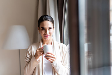 Happy young woman thinking and looking at side beside a window at home